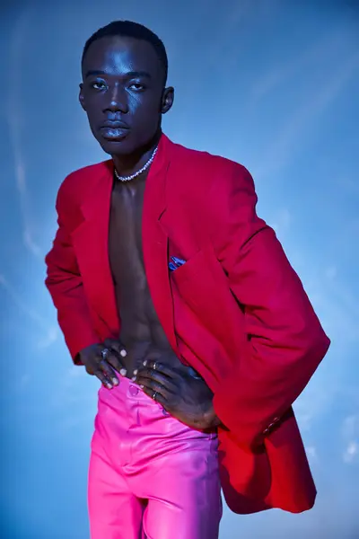 Привлечение стильный африканский американец в розовых штанах и красный блейзер позировать на голубом водянистом фоне — стоковое фото