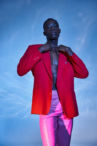 Спокусливий стильний афроамериканський чоловік в рожевих штанях і червоний блейзер позує на синьому водяному фоні — стокове фото