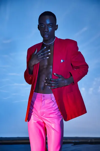 Charmant homme afro-américain élégant en pantalon rose et blazer rouge posant sur fond bleu aqueux — Photo de stock