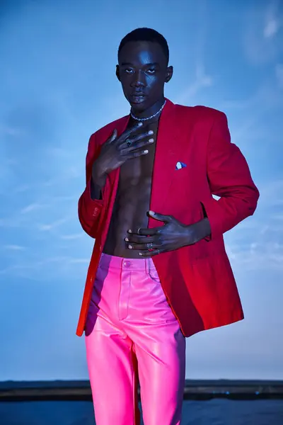 Handsome stylish african american man in pink pants and red blazer posing on blue watery backdrop — Stock Photo