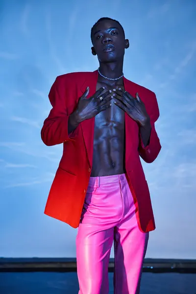 Handsome stylish african american man in pink pants and red blazer posing on blue watery backdrop — Stock Photo