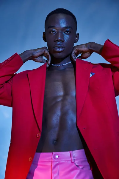 Handsome stylish african american man in pink pants and red blazer posing on blue watery backdrop — Stock Photo