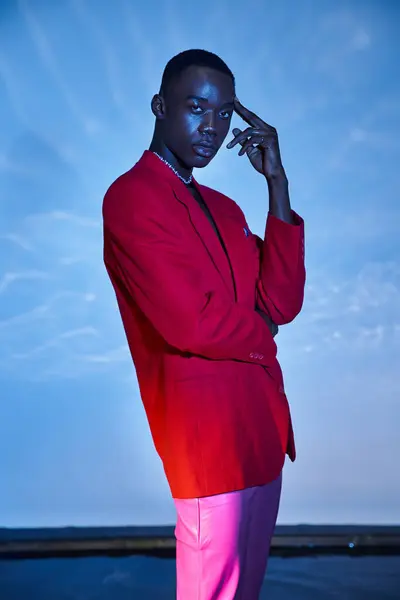 Appealing stylish african american man in pink pants and red blazer posing on blue watery backdrop — Stock Photo