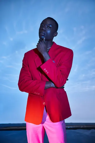Appealing stylish african american man in pink pants and red blazer posing on blue watery backdrop — Stock Photo