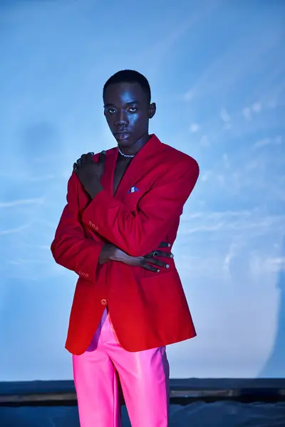 Alluring stylish african american man in pink pants and red blazer posing on blue watery backdrop — Stock Photo