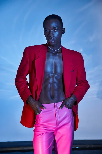 Модний афроамериканський чоловік в рожевих штанях і червоний блейзер дивиться далеко на водяний фон — стокове фото