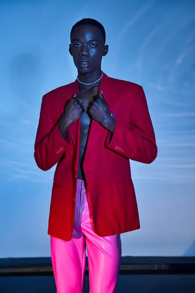 Alluring stylish african american man in pink pants and red blazer posing on blue watery backdrop — Stock Photo