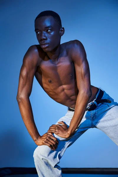 Trendy african american man in stylish jeans posing on blue watery backdrop and looking away — Stock Photo
