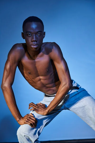 Enticing shirtless african american man in fashionable jeans looking at camera on watery backdrop — Stock Photo