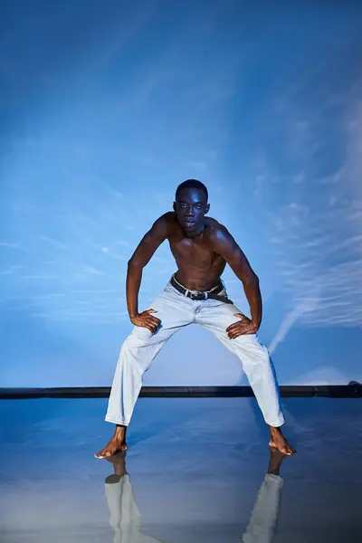 Verlockend hemdlos afrikanisch-amerikanischer Mann in modischen Jeans schaut in die Kamera vor wässriger Kulisse — Stock Photo