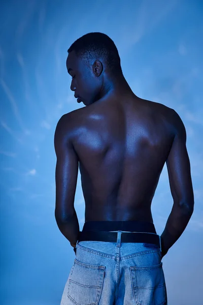 Back view of fashionable shirtless african american man in trendy jeans on blue watery backdrop — Stock Photo