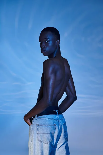 Спокусливий афроамериканський чоловік без сорочки в модних джинсах дивиться на камеру на водяному фоні — стокове фото