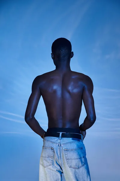 Rückansicht des modischen hemdlosen afrikanisch-amerikanischen Mannes in trendigen Jeans auf blauem wässrigem Hintergrund — Stockfoto