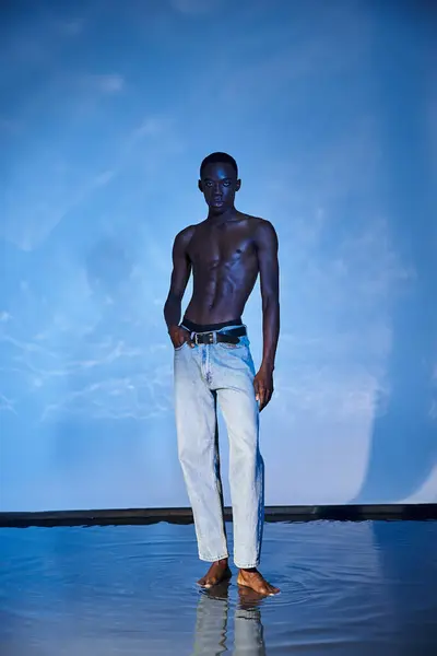 Charming shirtless african american man in fashionable jeans looking at camera on watery backdrop — Stock Photo