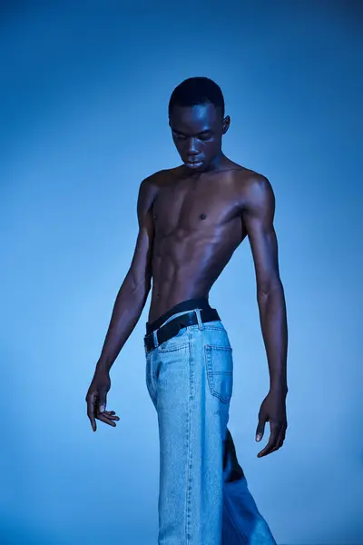 Young african american man in trendy jeans posing on blue watery backdrop and looking away — Stock Photo