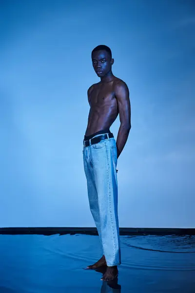 Handsome shirtless african american man in fashionable jeans looking at camera on watery backdrop — Stock Photo