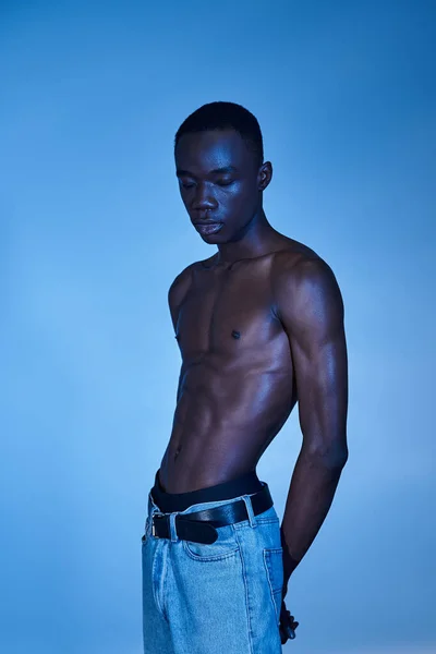 Shirtless african american man in trendy jeans posing on blue watery backdrop and looking away — Stock Photo