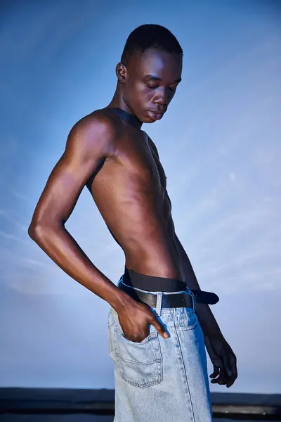 Homme afro-américain torse nu en jeans tendance posant sur fond bleu aqueux et détournant les yeux — Photo de stock