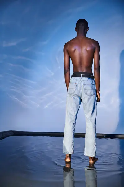 Back view of fashionable shirtless african american man in trendy jeans on blue watery backdrop — Stock Photo