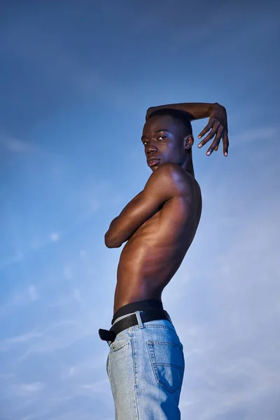 Attractive shirtless african american man in fashionable jeans looking at camera on watery backdrop — Stock Photo
