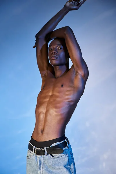 Sem camisa elegante homem americano africano em jeans elegantes e olhando para a câmera no fundo azul — Fotografia de Stock