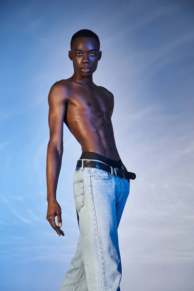 Shirtless trendy african american man in elegant jeans and looking at camera on blue background — Stock Photo