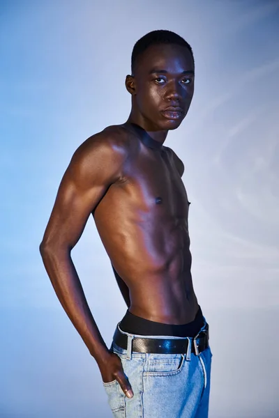 Sem camisa na moda homem americano africano em jeans modernos e olhando para a câmera no fundo azul — Fotografia de Stock