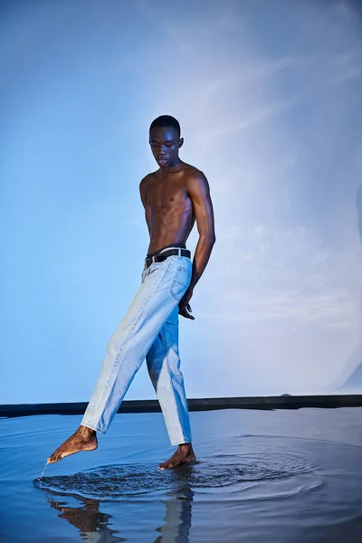 Attraktive junge afrikanisch-amerikanische Mann in stylischen Jeans posiert oben ohne auf wässrigem blauem Hintergrund — Stockfoto