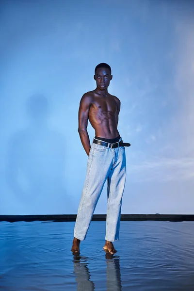 Shirtless stylish african american man in modern jeans and looking at camera on blue background — Stock Photo