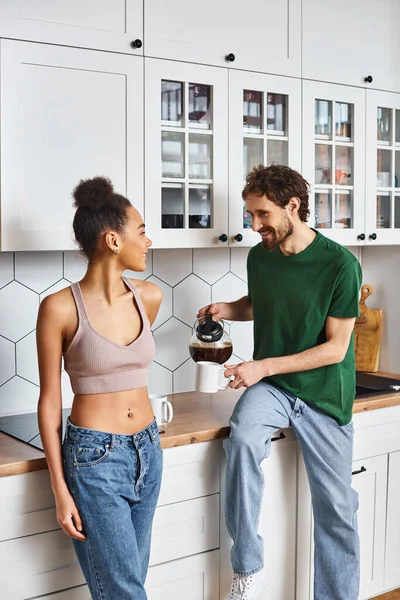Good looking jolly interracial couple in homewear enjoying each other and drinking coffee in kitchen — Stock Photo