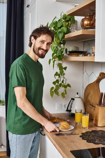 Good looking joyous man in comfy homewear holding croissants and looking at camera happily — Stock Photo