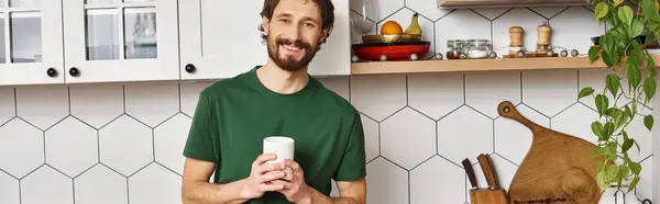 Handsome jolly man in homewear holding cup with hot coffee and smiling at camera joyfully, banner — Stock Photo