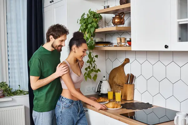 Handsome man hugging his african american beautiful girlfriend while she holds croissants at home — Stock Photo
