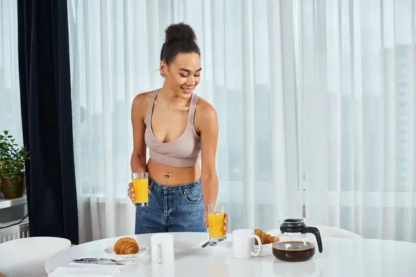 Attraktive junge afrikanisch-amerikanische Frau in Homewear serviert Orangensaft zum Frühstück zu Hause — Stockfoto
