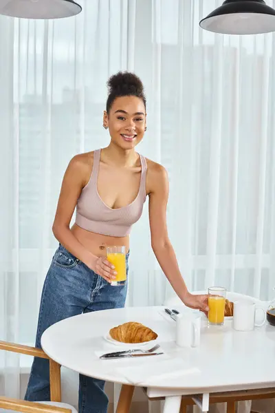 Schöne fröhliche afrikanisch-amerikanische Frau in Homewear serviert Orangensaft und lächelt in die Kamera — Stockfoto