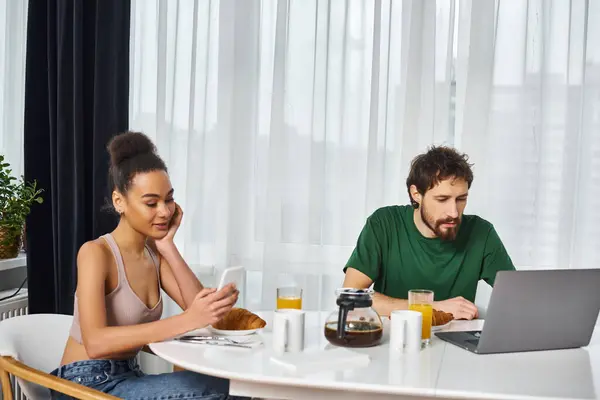 Atraente mulher afro-americana olhando para o telefone, enquanto seu namorado olhando para laptop no café da manhã — Fotografia de Stock