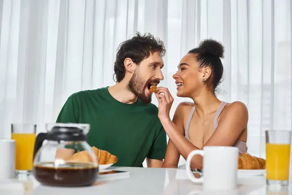 Alegre atraente mulher afro-americana em traje casual alimentação croissant para seu namorado alegre — Fotografia de Stock