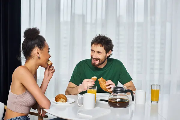 Appealing multicultural jolly couple in homewear having delicious breakfast together at home — Stock Photo