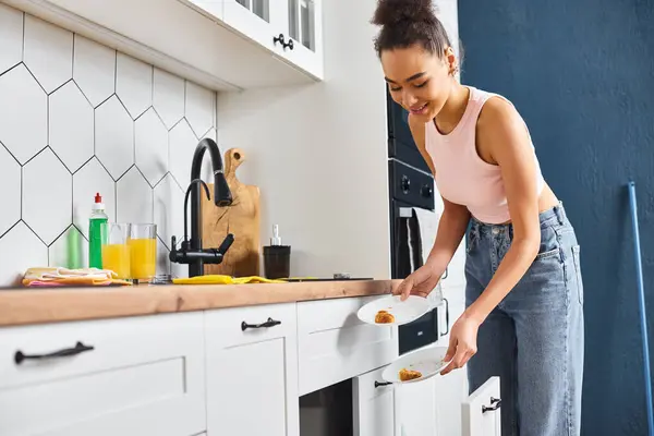 Bien parecido alegre africana americana mujer en la limpieza de la ropa de casa platos después del desayuno en casa - foto de stock