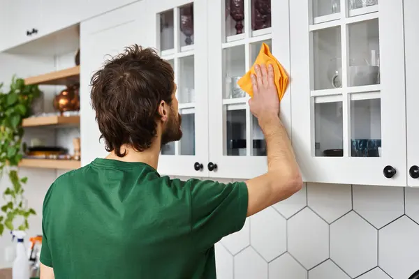Back view of man in casual dark green t shirt using rag to clean kitchen cupboards while at home — Stock Photo