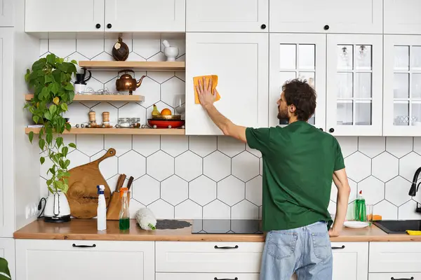 Back view of man in comfy green t shirt using yellow rag to clean kitchen cupboards at home — Stock Photo