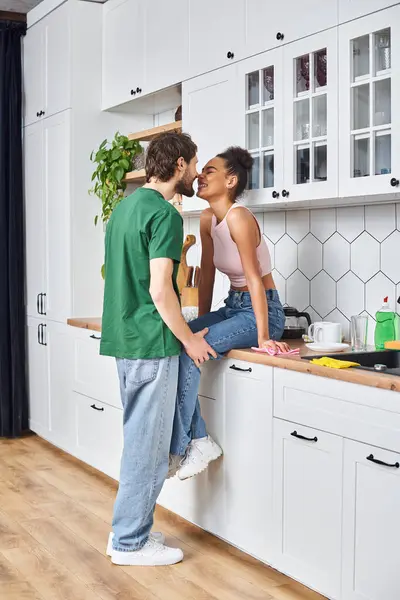 Beautiful african american woman sitting on counter next to her jolly handsome boyfriend at home — Stock Photo