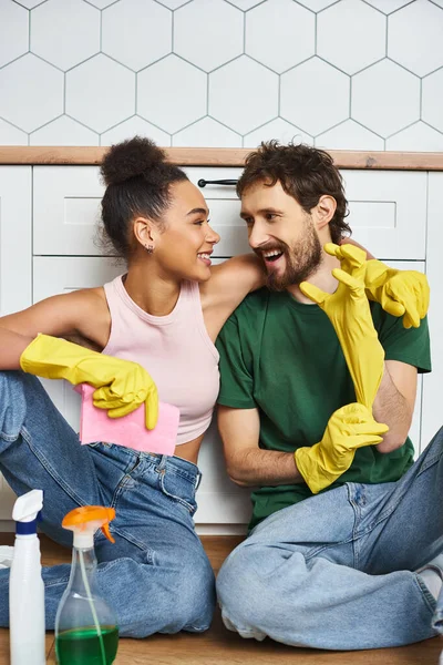 Loving cheerful multicultural couple in comfy homewear sitting on floor during spring cleaning — Stock Photo