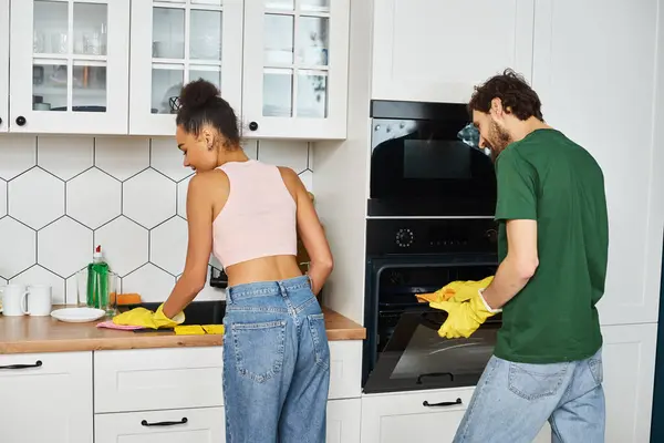 Alegre hermosa pareja interracial en la ropa de casa limpieza de sus utensilios de cocina con atención en casa - foto de stock