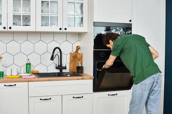 Hombre atractivo en traje acogedor diario con guantes usando trapo para lavar el horno durante la limpieza de primavera - foto de stock