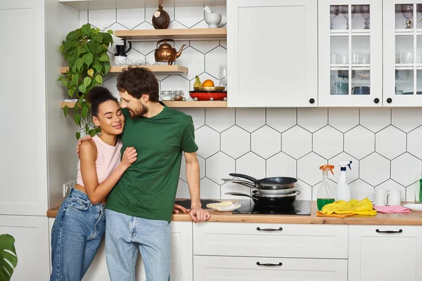 Beautiful cheerful diverse couple in cozy homewear enjoying each other and smiling happily — Stock Photo