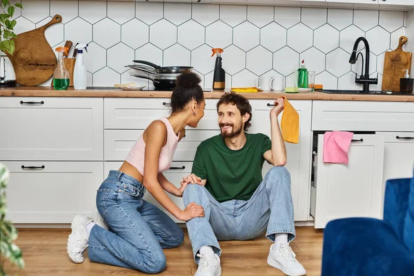 Good looking diverse jolly couple in homewear sitting on floor during cleaning and smiling happily — Stock Photo