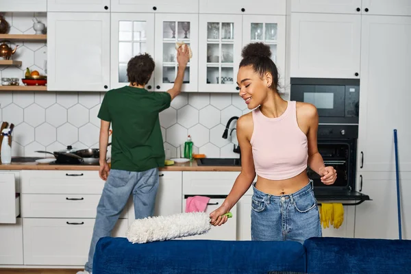 Cheerful multicultural couple in cozy homewear doing their chores at home during spring cleaning — Stock Photo
