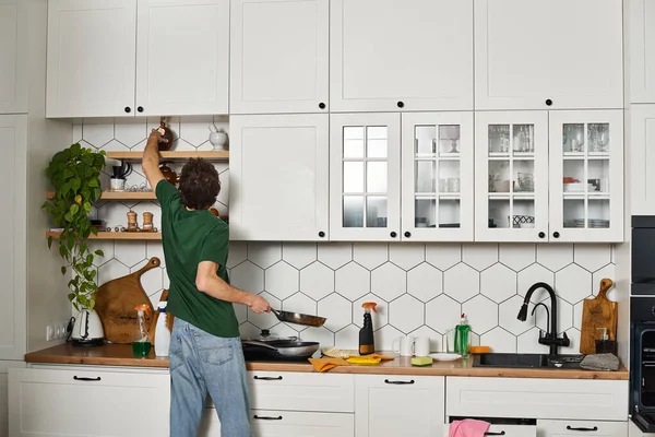 Vista trasera del hombre en camiseta casual verde oscuro haciendo tareas en la cocina durante la limpieza de primavera - foto de stock