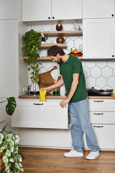 Schöner Mann in dunkelgrünem, gemütlichem T-Shirt, der Hausarbeit macht und beim Frühjahrsputz Lappen in der Hand hält — Stockfoto